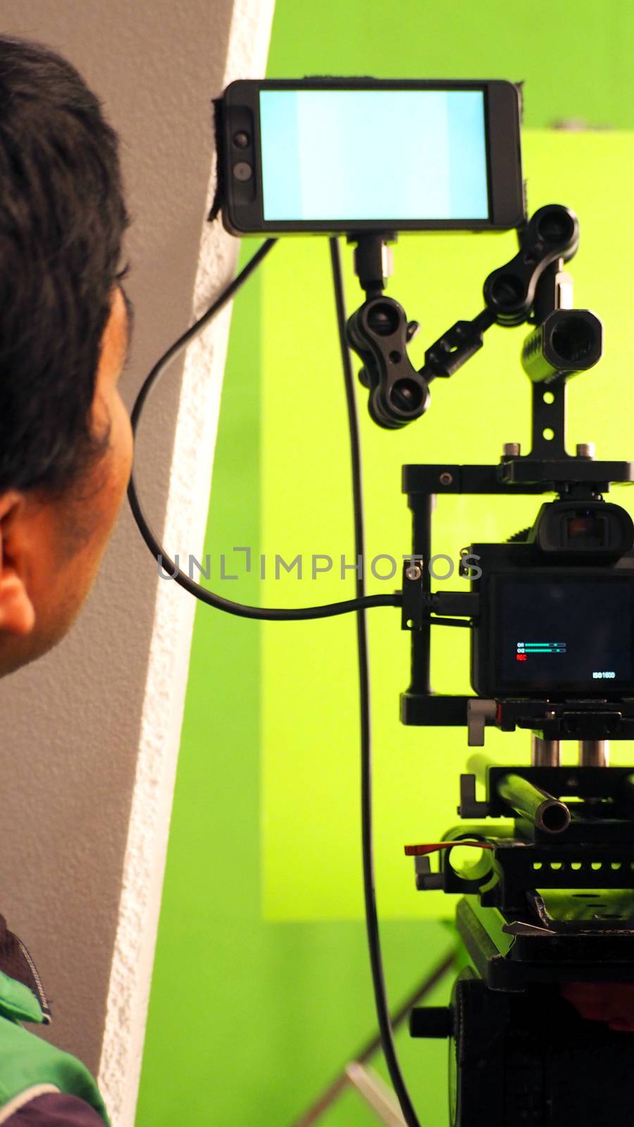 Behind the vdo camera in studio production that shooting or filming green screen background for chroma key technique in post process with professional crew teams and equipments.