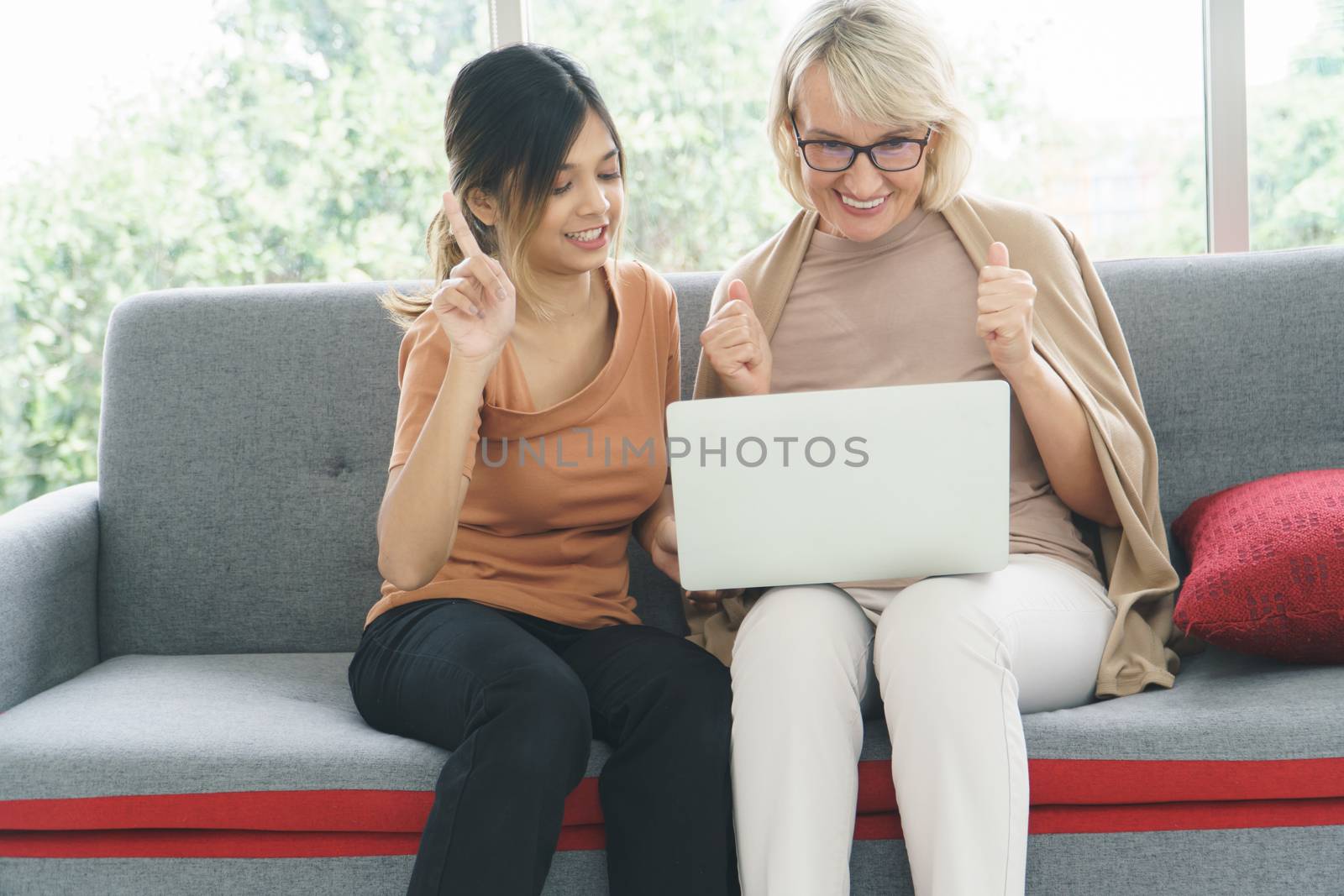 happy grandmother and grown granddaughter are fun and laughing. older mother and daughter use technology to learn on laptop together.  concept Family, mix skin, love, care, share time, and adoption.