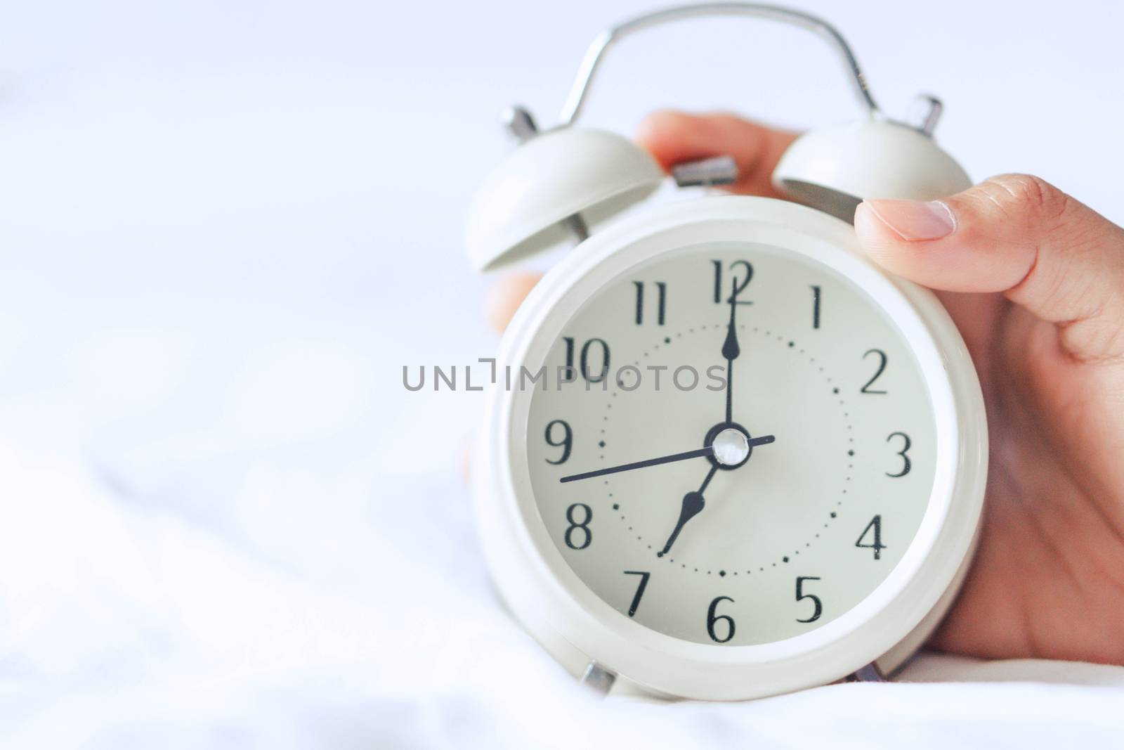 Closeup hand holding alarm clock on white bed, Time to wake up by pt.pongsak@gmail.com