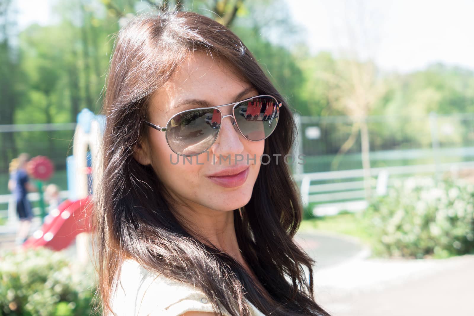 Young brunette woman with natural make-up, smiling with sunglasses in the park. Defocused blurry background.