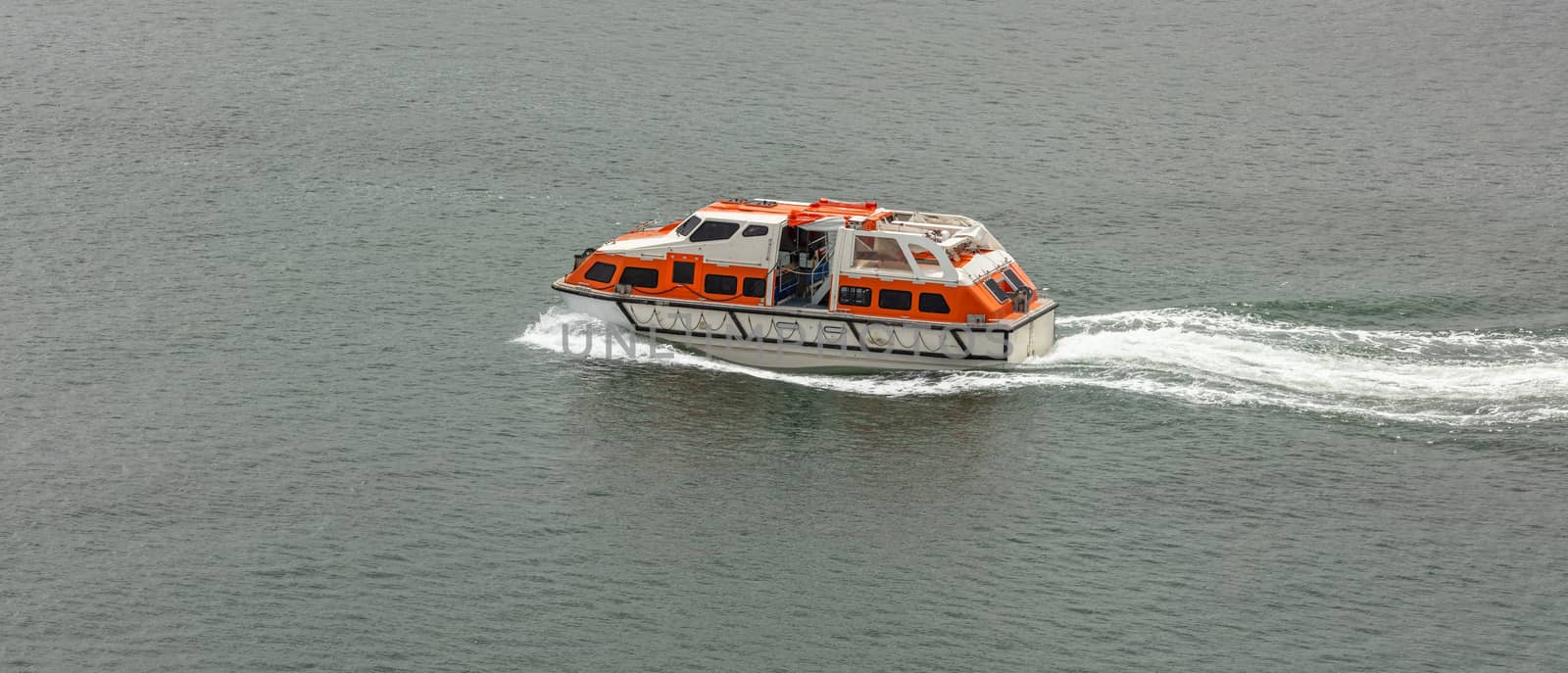 Orange-and-white life boat moving fast in the water. Life saving equipment concept.
