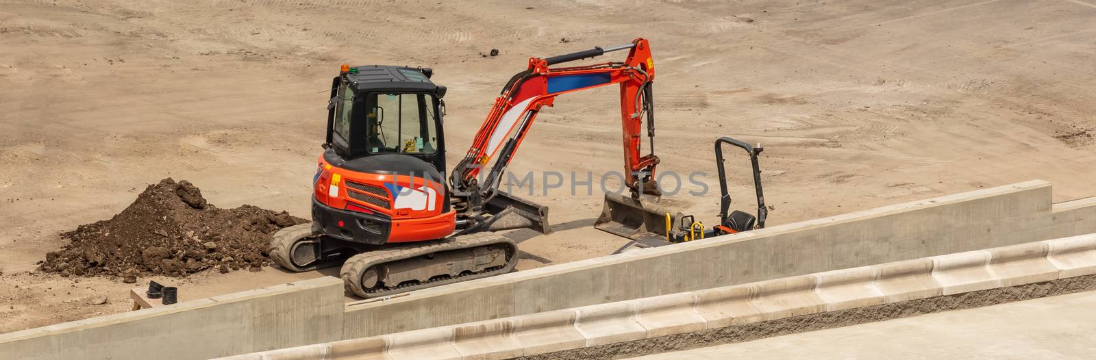 Orange excavator parked next to a concrete platform. Construction site. Aerial angled view.