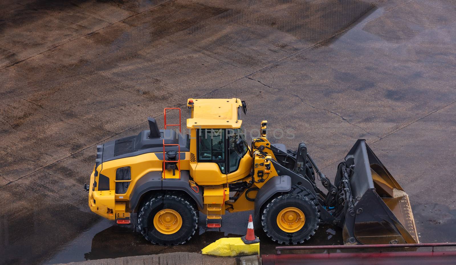 Heavy yellow bulldozer parked on wet concrete surface. Industrial site.