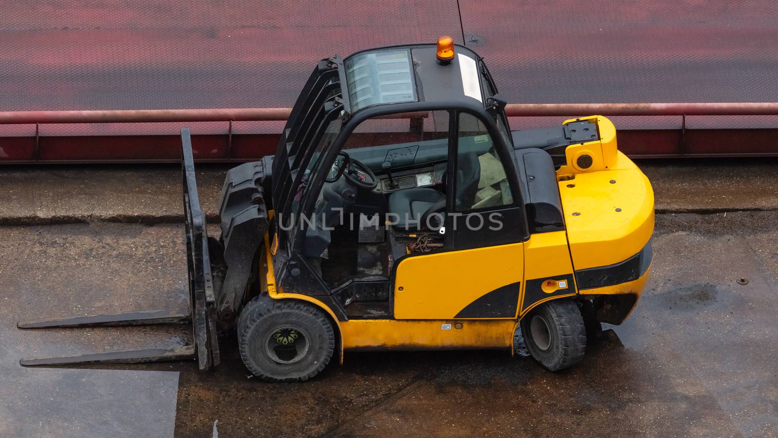 Yellow forklift parked on wet concrete surface. by DamantisZ