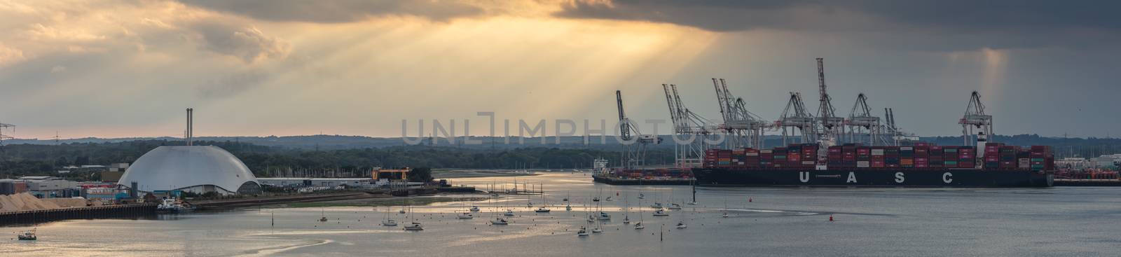 Southampton port, England, UK - June 08, 2020: Aerial panoramic view of Southampton port at sunset. Golden hour. Massive container ship UASC being loaded; yacht lot, metal factory dome in the middle