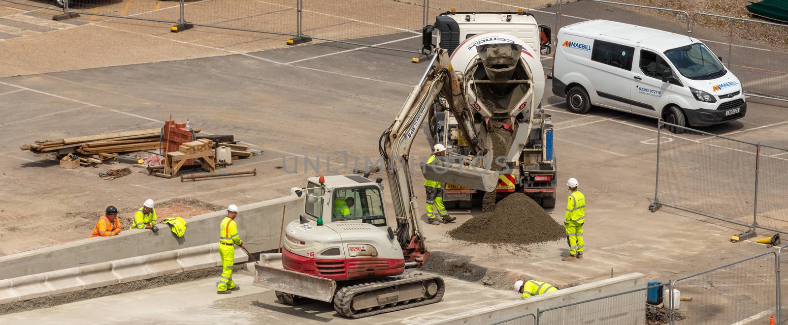 Southampton port, England, UK - June 08, 2020: Construction workers wearing light green safety clothing and hard hats on site. Excavator, concrete mixer. Construction concept.