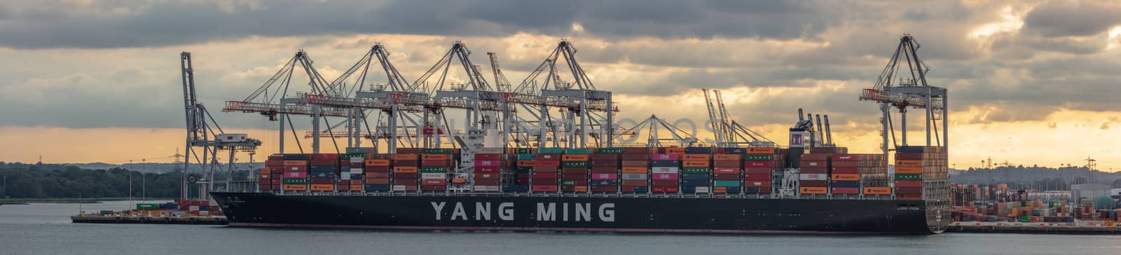 Southampton, UK - June 11, 2020: Panoramic aerial view of huge container ship Yang Ming being loaded with containers in the port of Southampton at sunset. Golden hour.