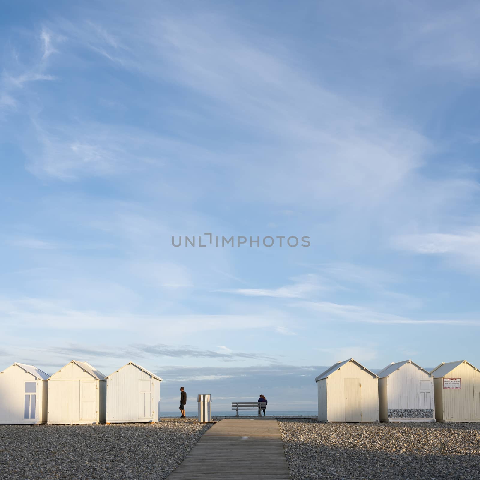 cayeux, france, 6 august 2020: people near beach huts in cayeux s mer in french normandy under blue sky in early morning sunlight