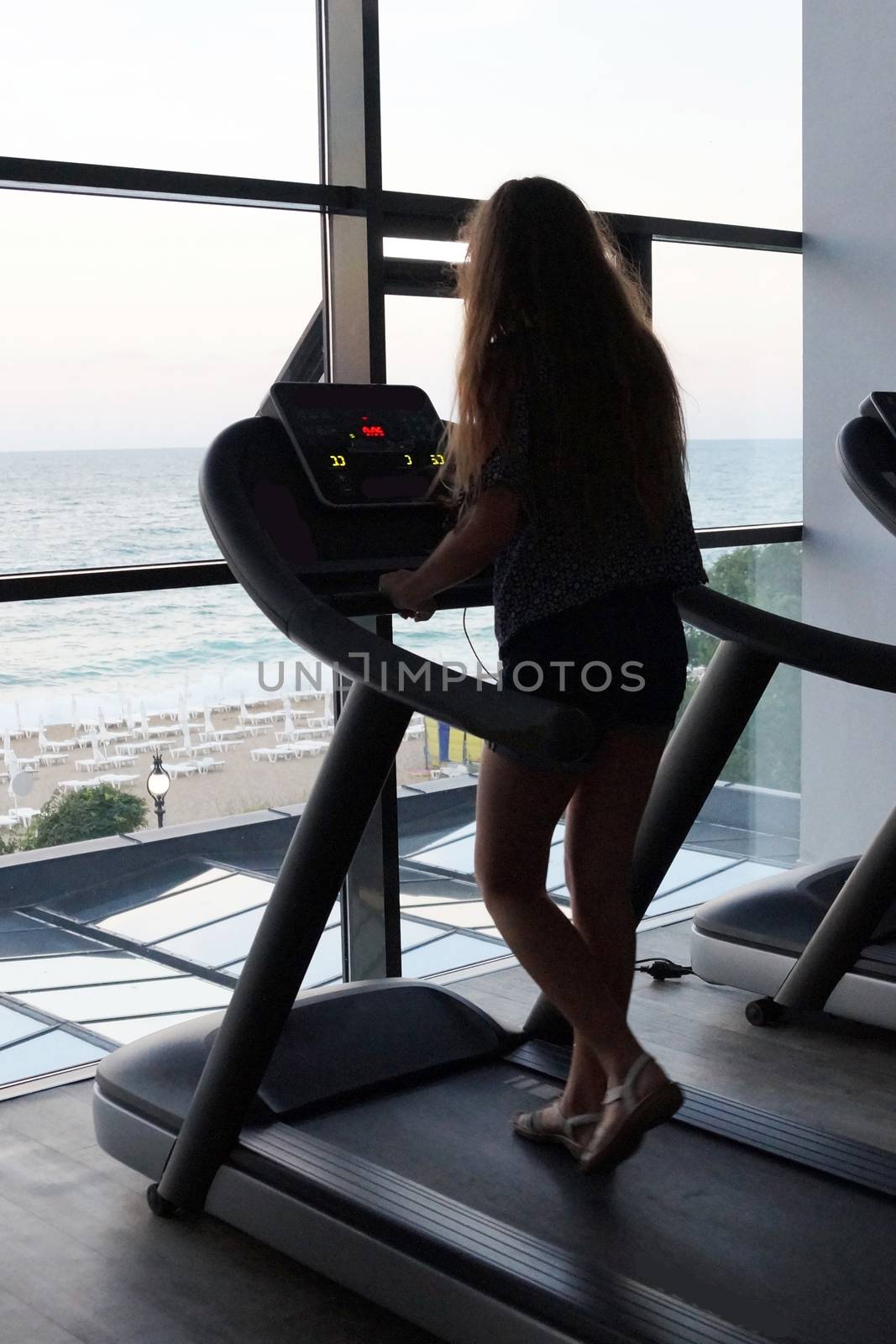 tteenage girl on a treadmill in the gym in front of the window with a sea view, back view.