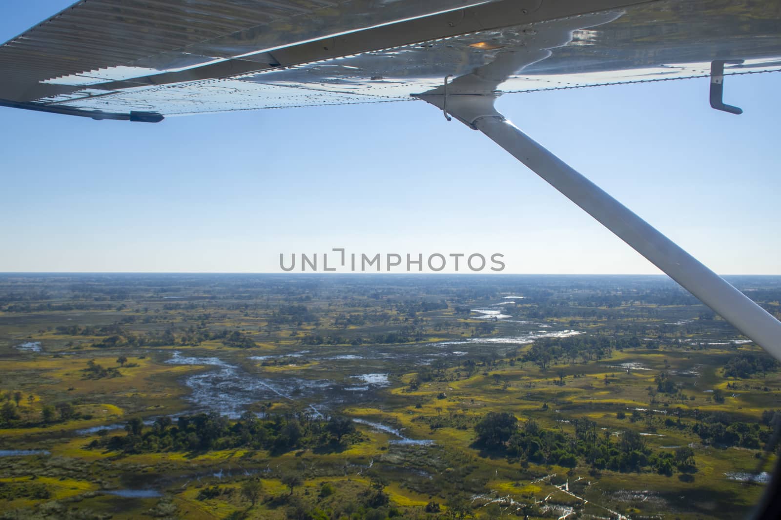 Aerial view at Moremi national park in Botswana, Africa, as seen from a small aircraft. Wing visible, bright sunshine on blue sky. Travel and Tourism