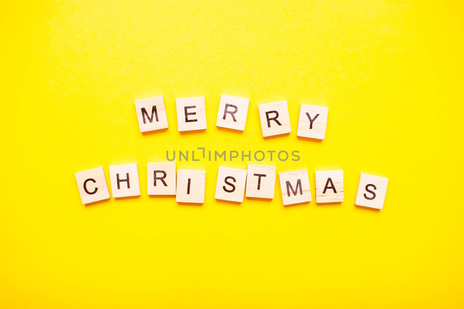 The inscription merry christmas made of wooden blocks on a light yellow background.