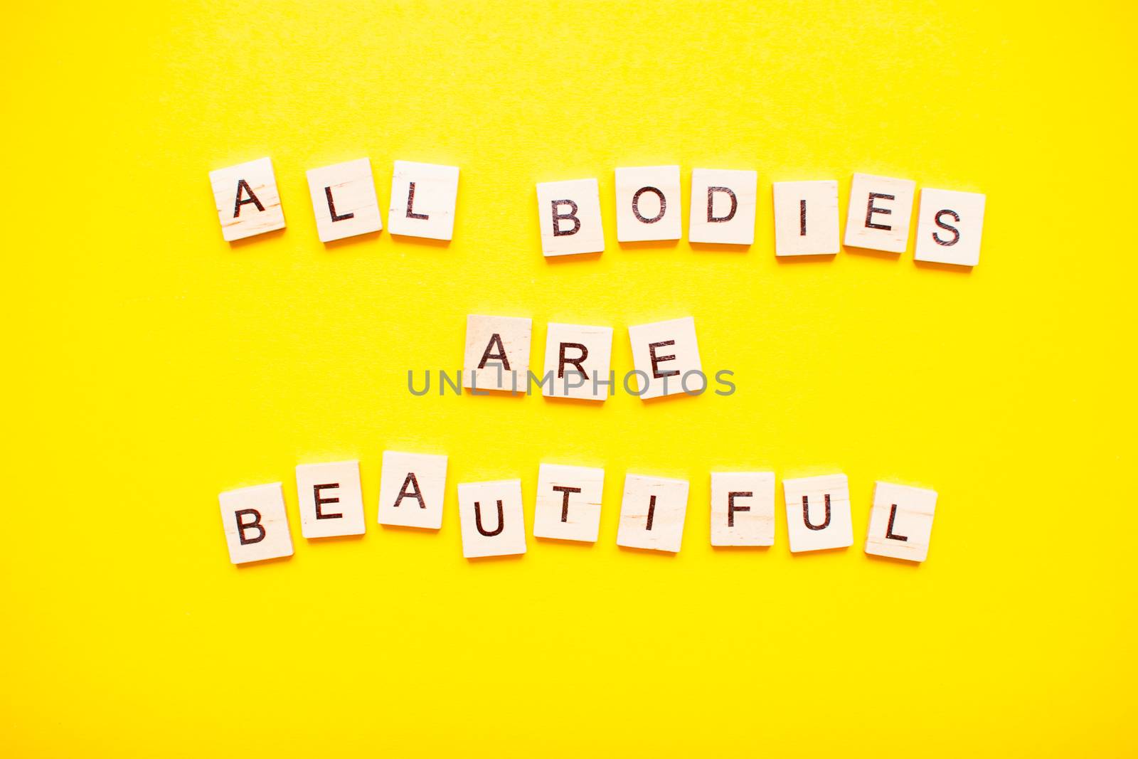 The inscription all bodies are beautiful made of wooden blocks on a light yellow background.