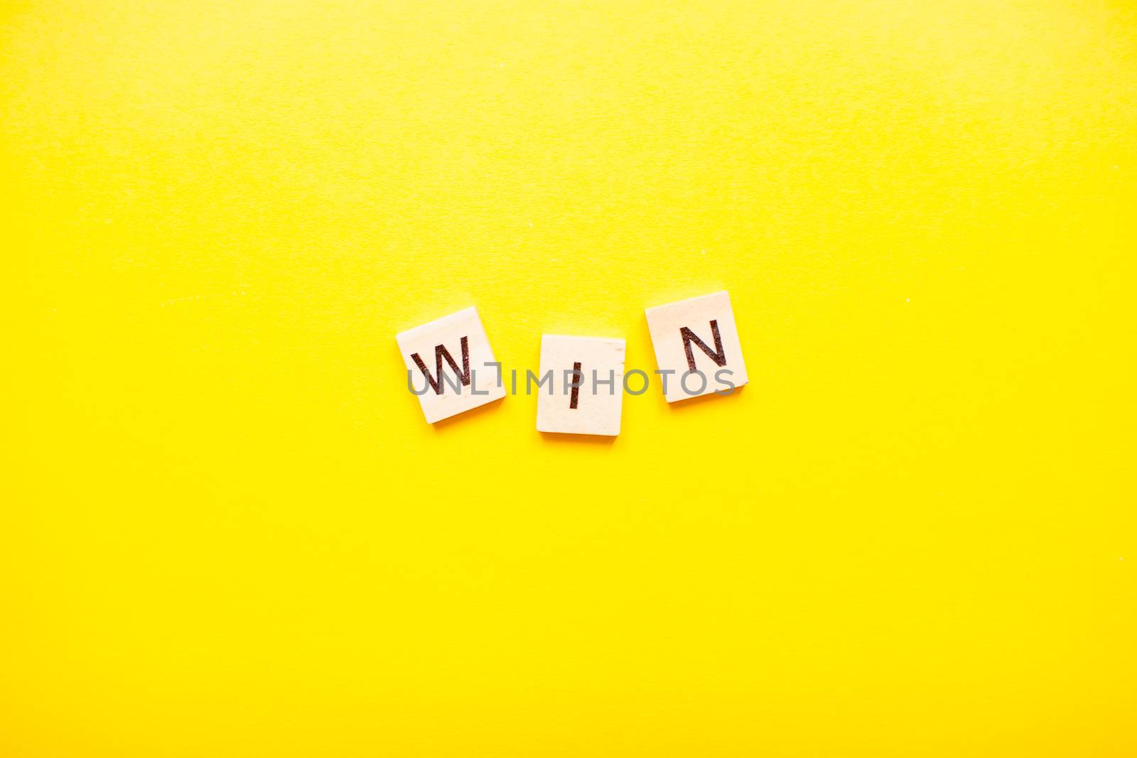 The inscription win made of wooden blocks on a light yellow background.