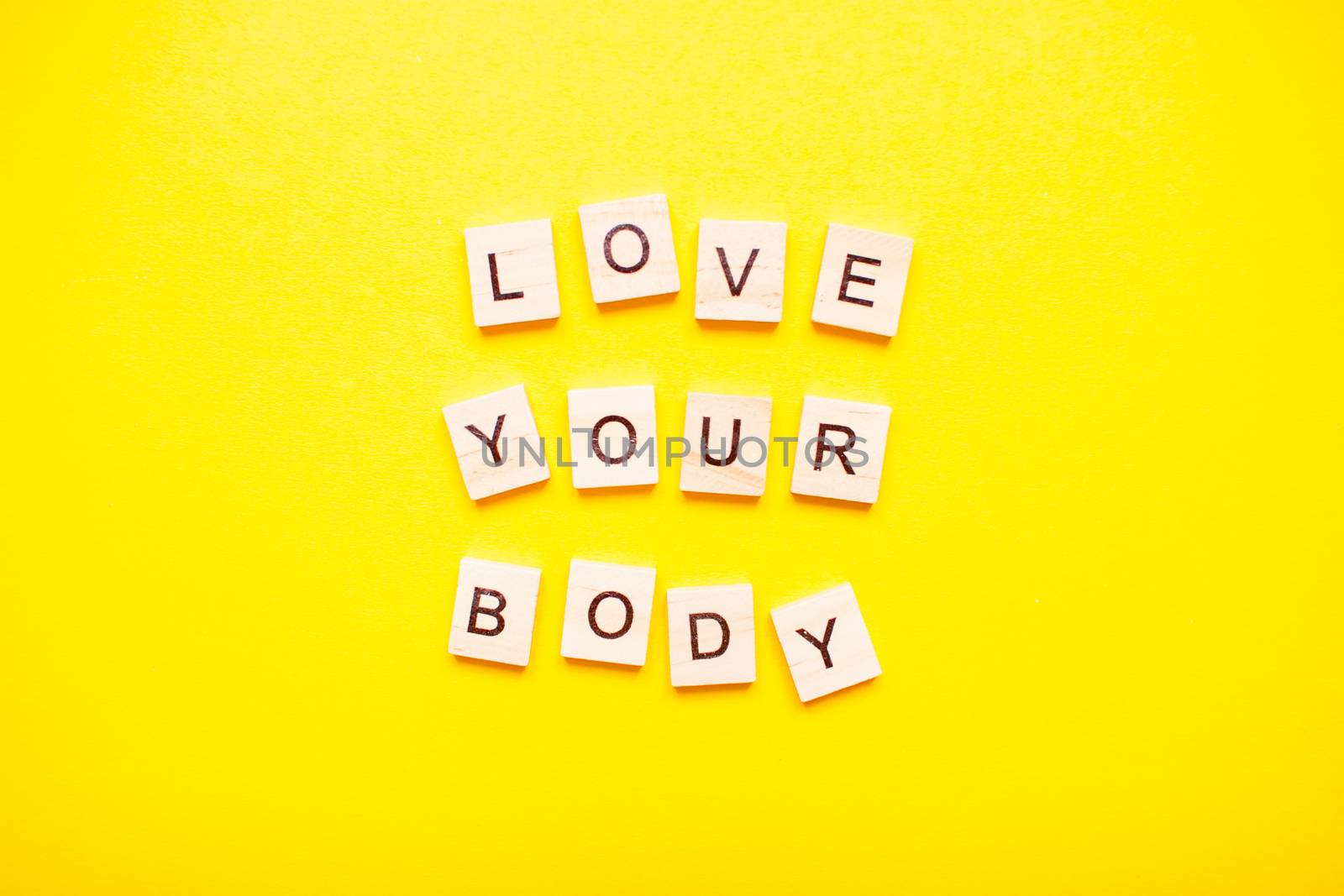 The inscription love your body made of wooden blocks on a light yellow background.