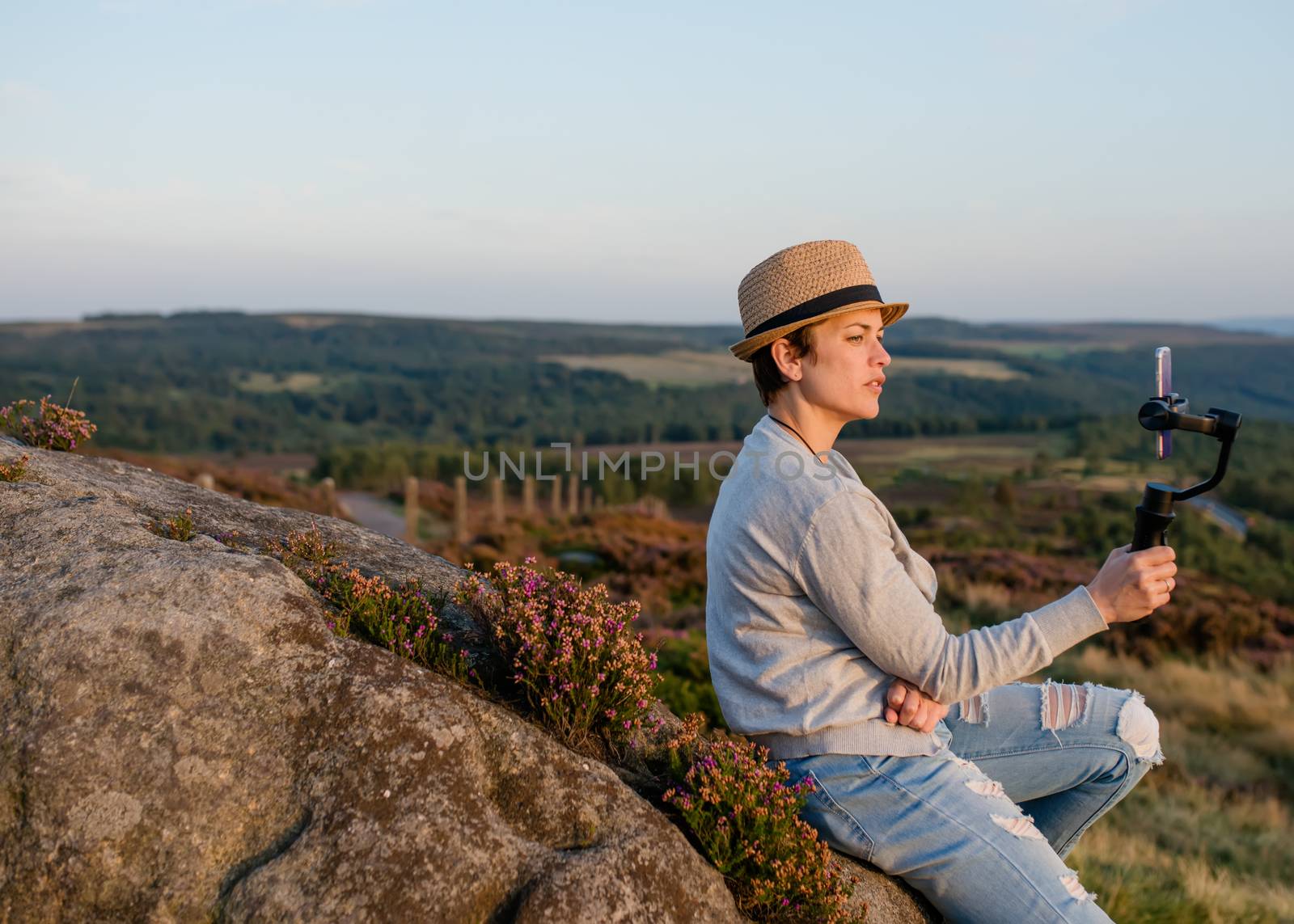A woman sitting on top of hill and taking photos on phone against an amazing landscape in the autumn