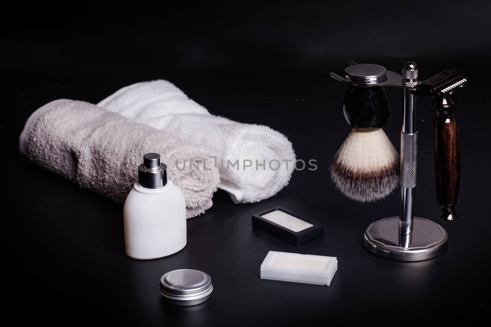 Razor and brush on stand, towels, perfume, balsam and blades on a black background.