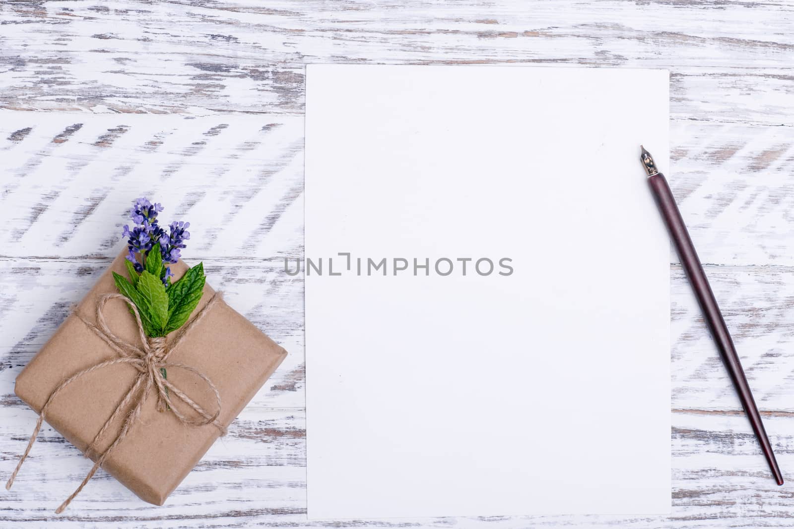 Mock up of empty paper, flower, ink pen, and gift on white wood desk. Flat Lay with no people. View from the top.