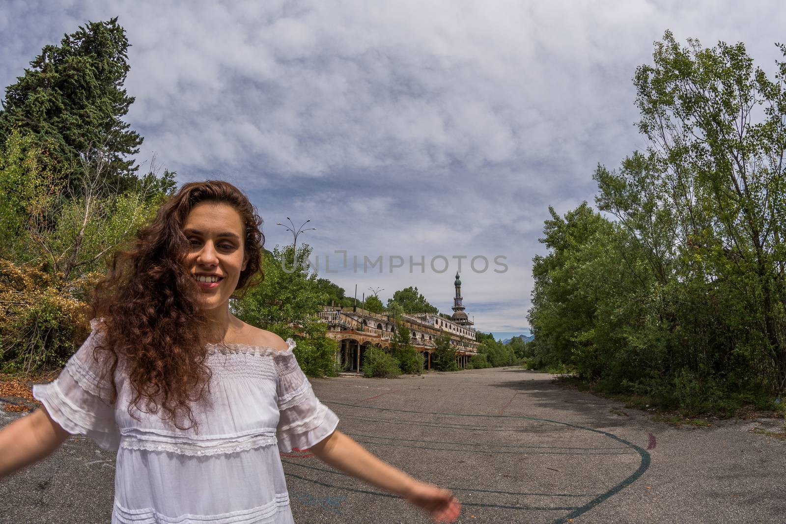 Beautiful young woman in light dress posing standing in front of the ruins of a ghost town