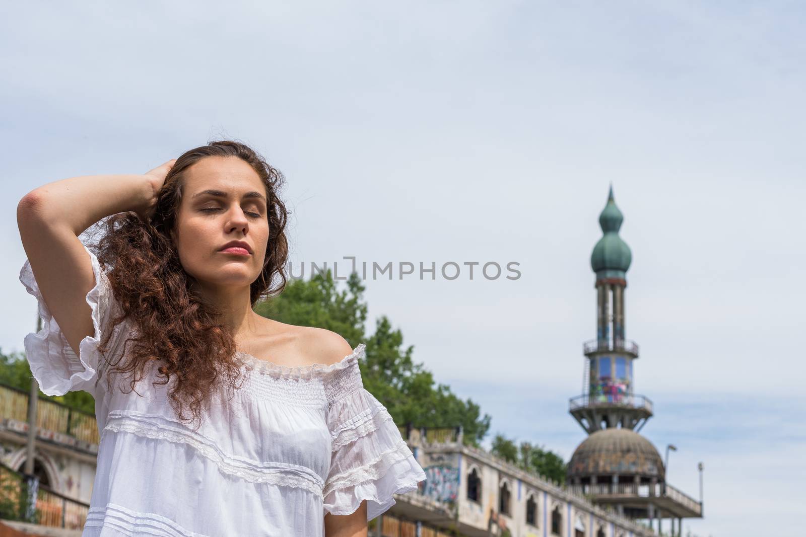 Beautiful young woman in light dress posing standing in front of the ruins of a ghost town