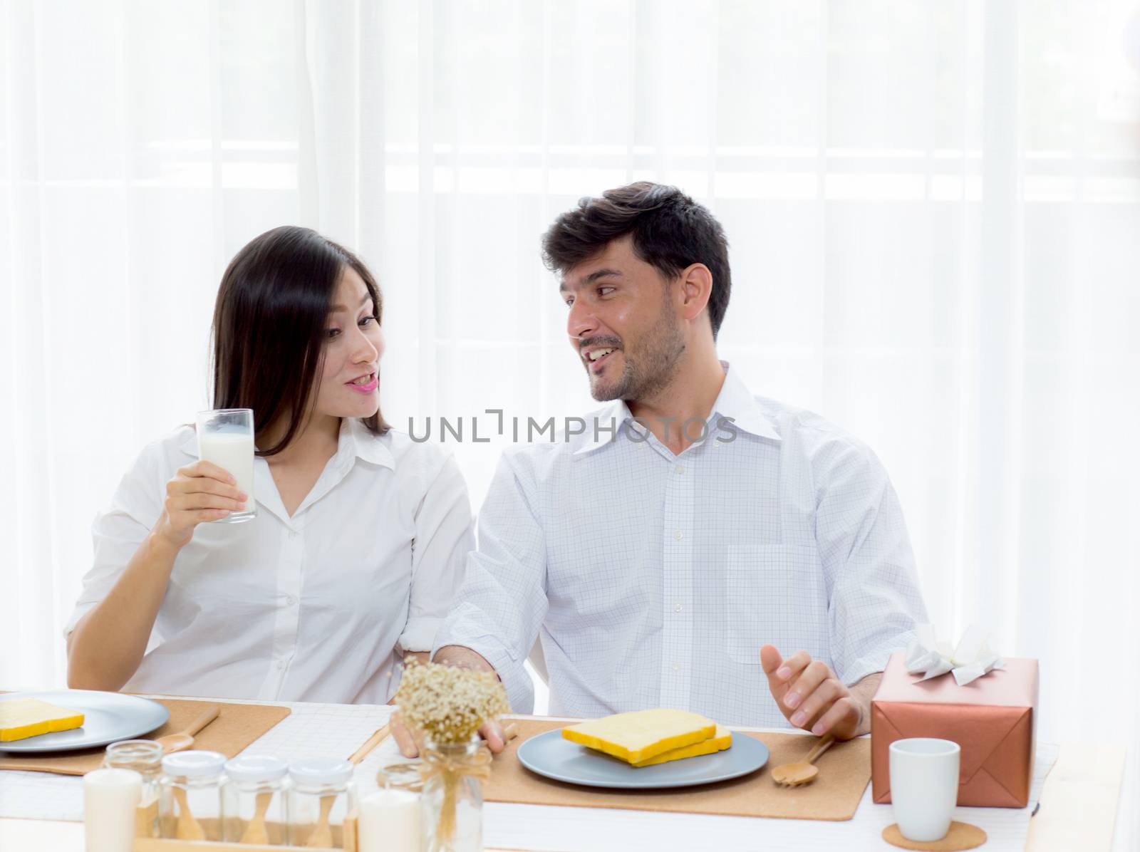 Cheerful asian young man and woman having sitting lunch and talking  together at kitchen