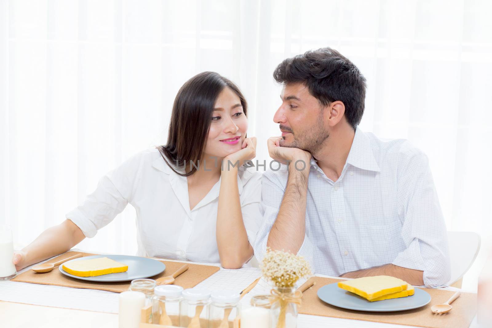 Cheerful asian young man and woman having sitting lunch and talking together at kitchen, family relationship with romantic concept.