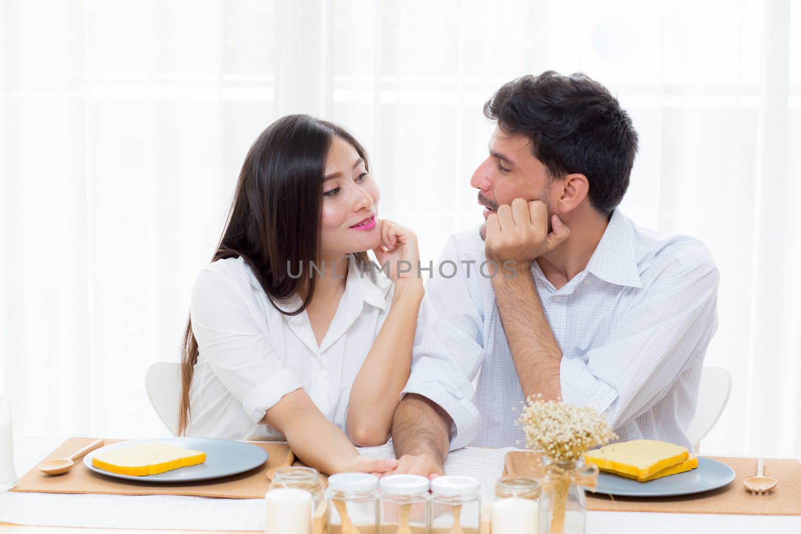 Cheerful asian young man and woman having sitting lunch and talking  together at kitchen
