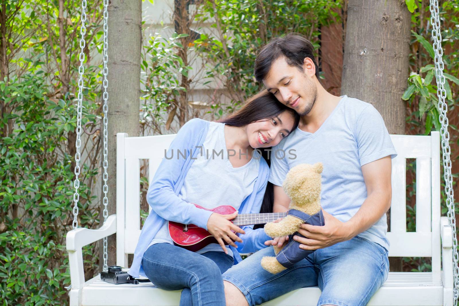 Young asian woman and man couple sitting at park playing ukulele and sing a song outdoors relax concept.