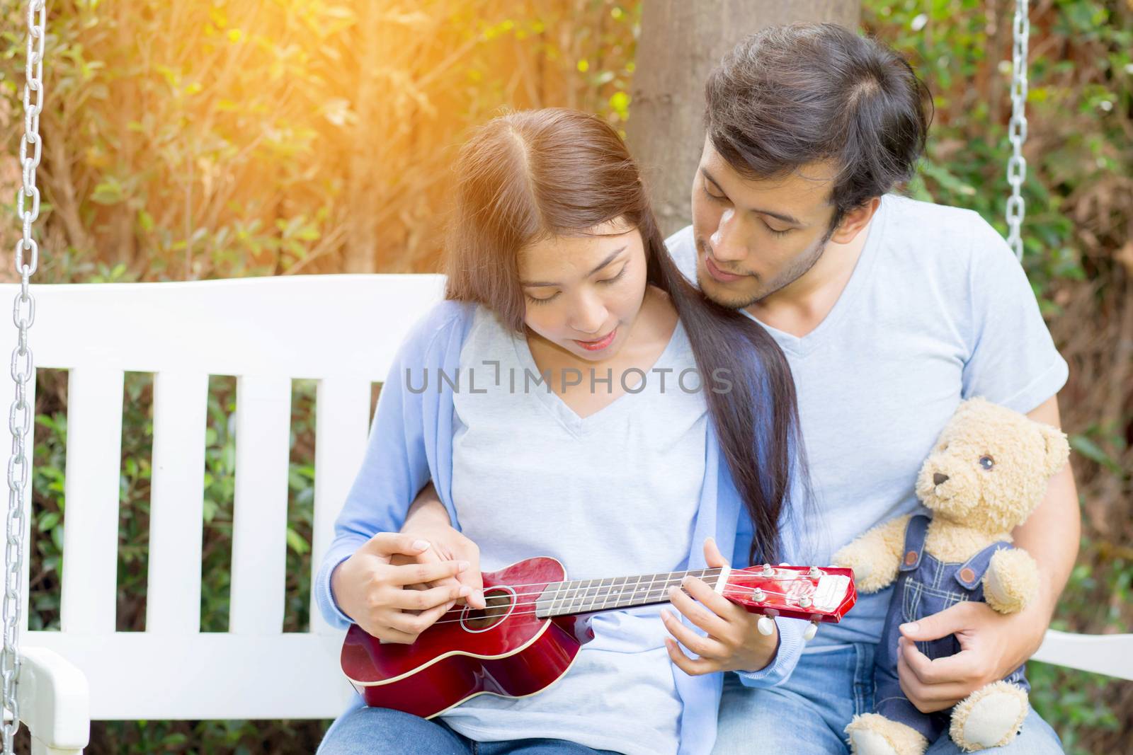 Young asian woman and man couple sitting at park playing ukulele and sing a song outdoors relax concept.