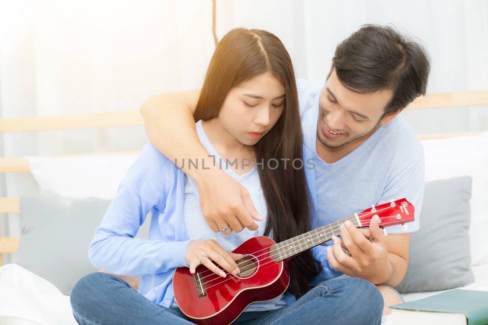Young Asian couple playing ukulele relaxing with happiness and joyful in bedroom.