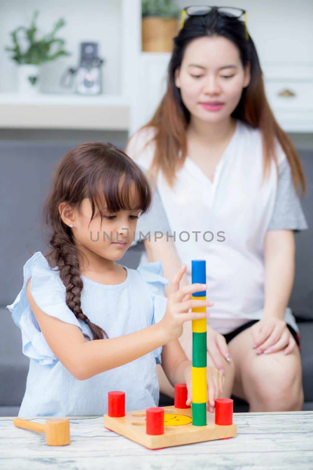 Asian kid girl and mother playing toy block; together with cheerful and happy in living room, activity in family.