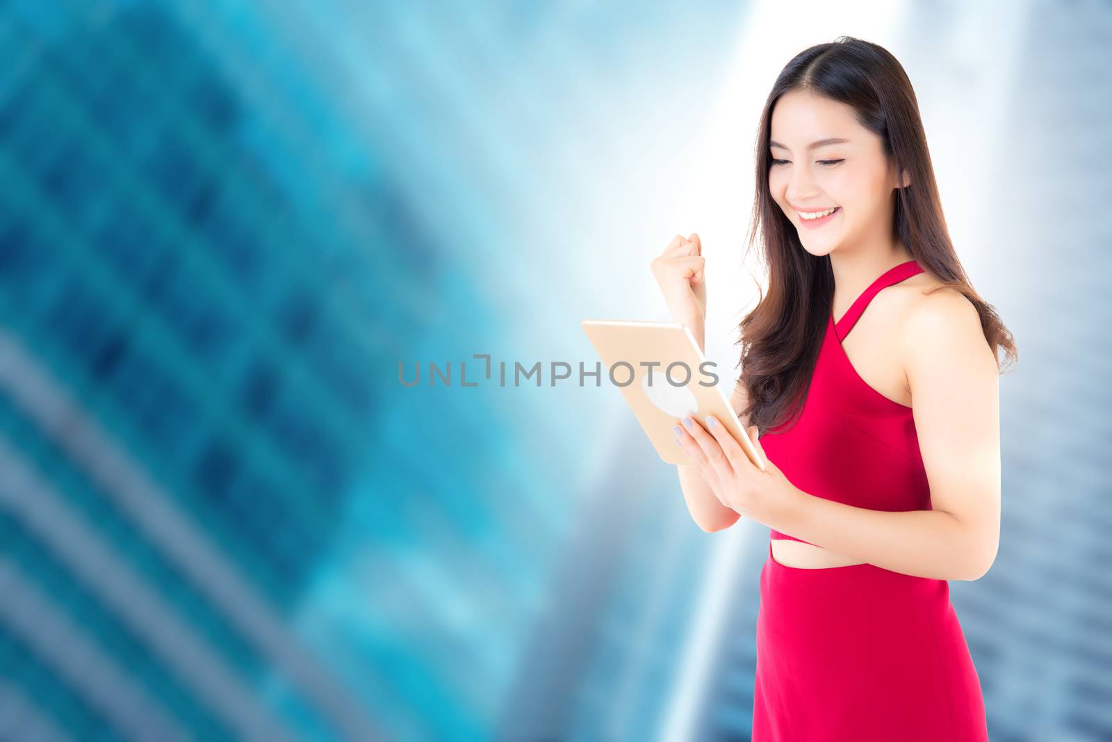 Young beautiful asian woman wear red dress looking on tablet with happy and success gesture glad on city background - communication business concept.