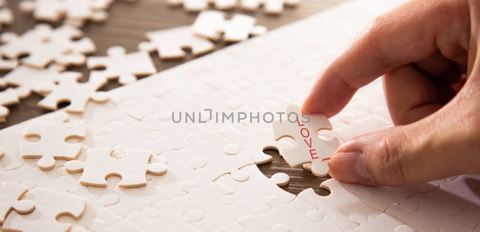 Hand completing the a last piece of jigsaw puzzle with love word by tehcheesiong