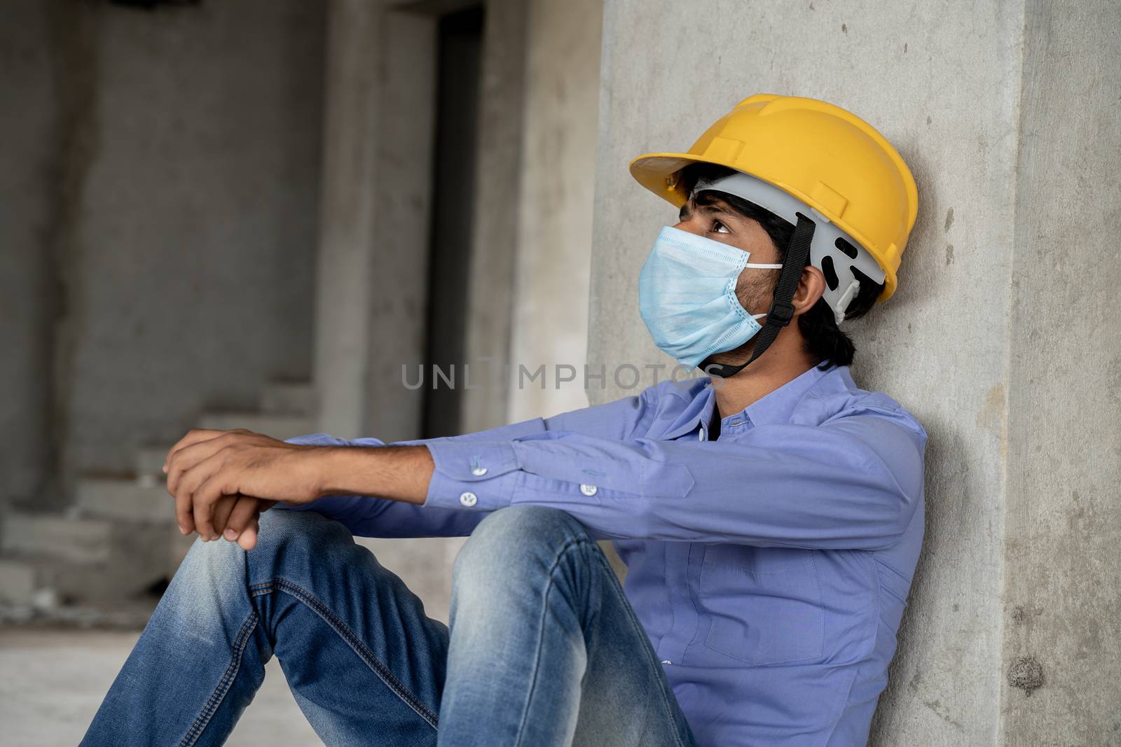 Head shot side view of construction worker seeing outside from construction building window in sad - Industrial worker in a hardhat with medical mask due to coronavirus or covid-19 crisis. by lakshmiprasad.maski@gmai.com