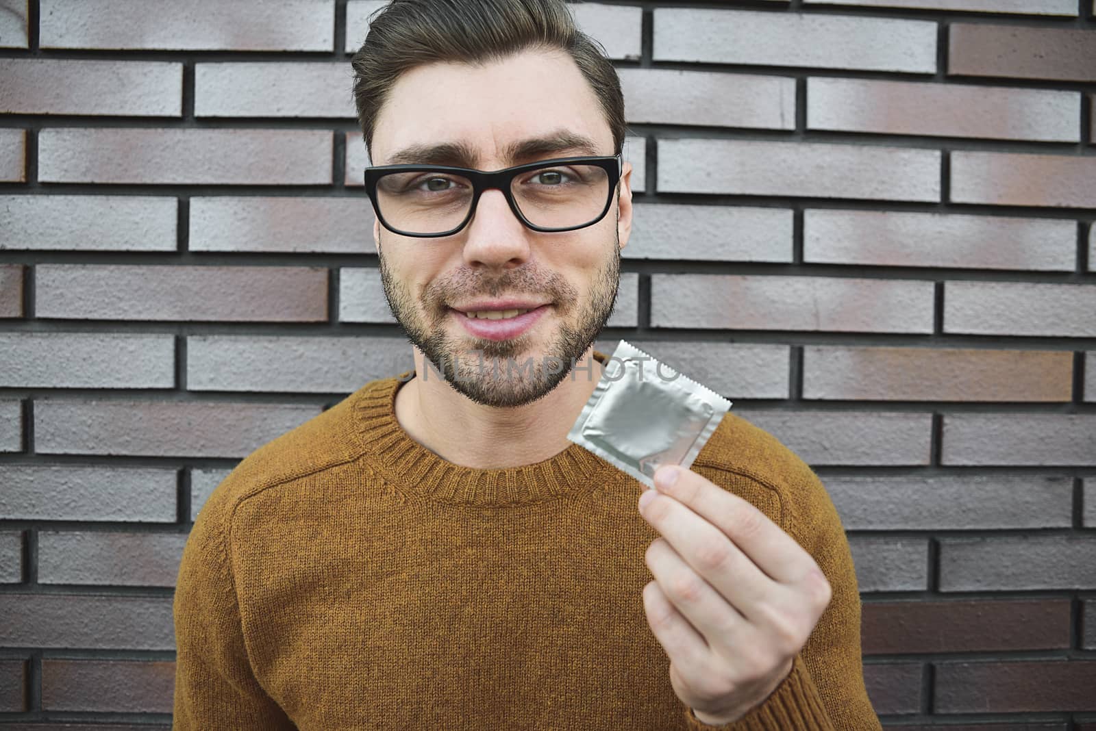 Male youngster with appealing look, holds condom.