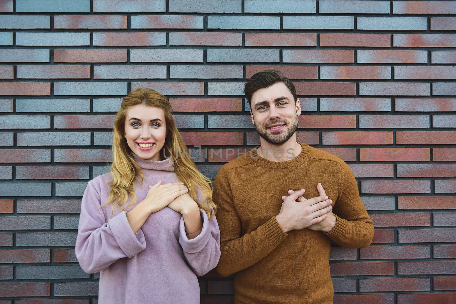 Graceful cheerful positive young woman and man have satisfied expressions, keep both hands on heart, feel thankful to guests, being in high spirit, stand against white background. by Nickstock