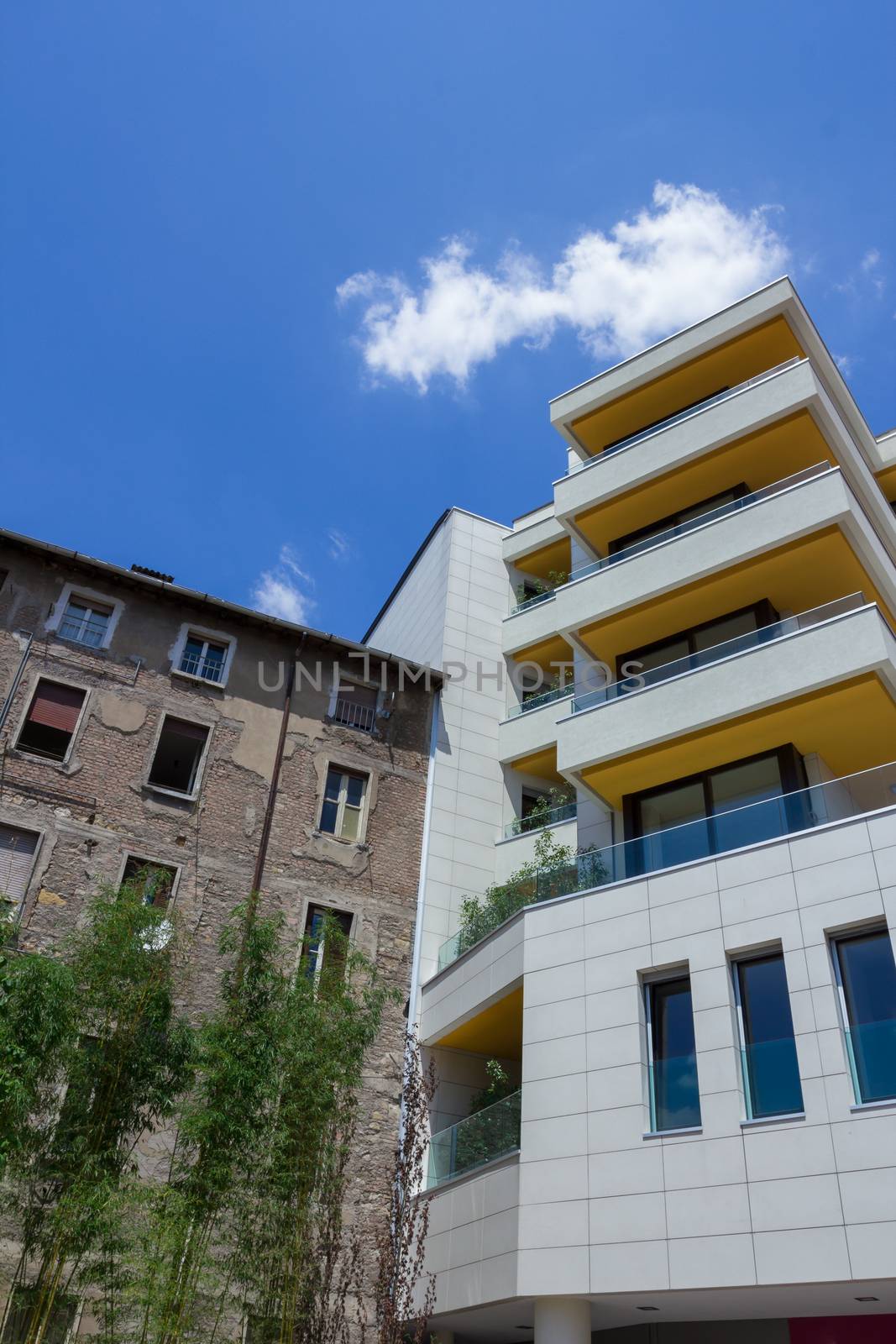New tall apartment house build near a small and old apartment. Blue sky with white clouds. Concept of old and new.