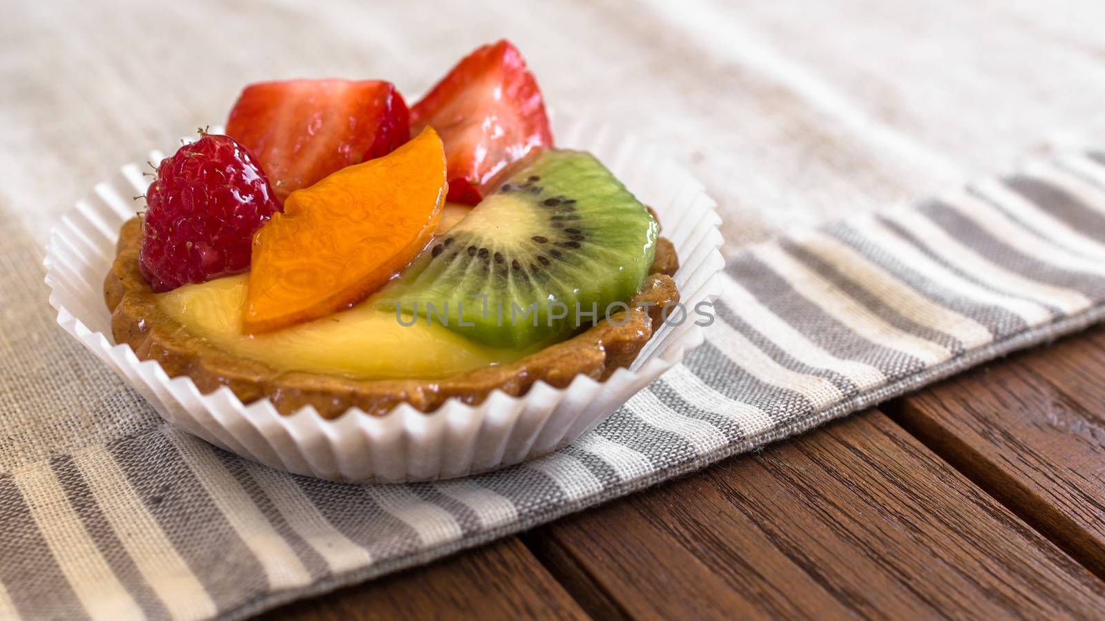 A cake with cream and mixed fruit, resting on linen tablecloth.