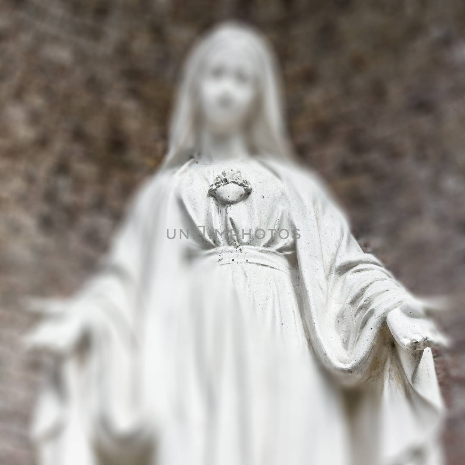 Blurred image of Virgin Mary statue. Selected focus on her hand and heart.