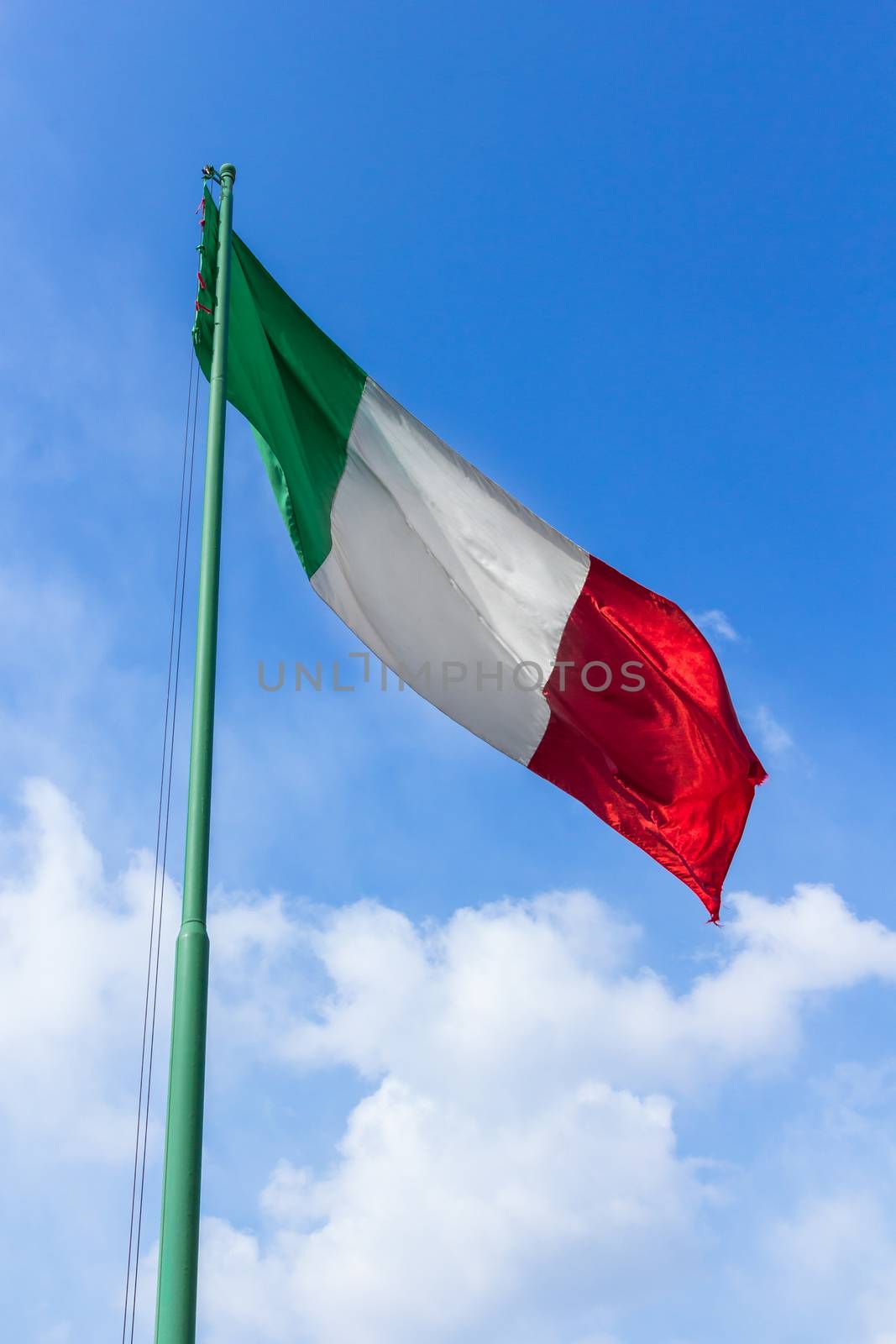 Italy flag waving against blue sky with white clouds.