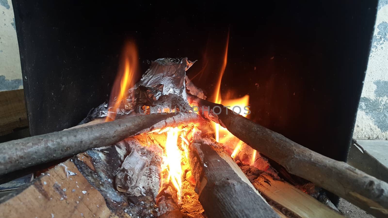 Fire on logs in fire pot with embers and burning coal. Bonfire with blazing red and orange fire flames. Fire background with woods and planks on fire at night view.