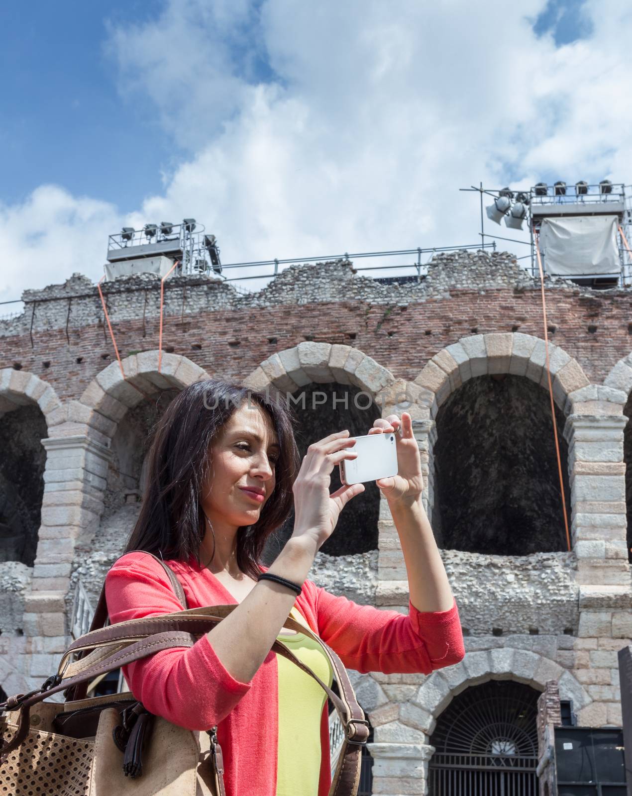 Female tourist taking a photo with mobile phone while sightseeing the city of Verona (Italy) with famous Arena on background. Shallow DOF.