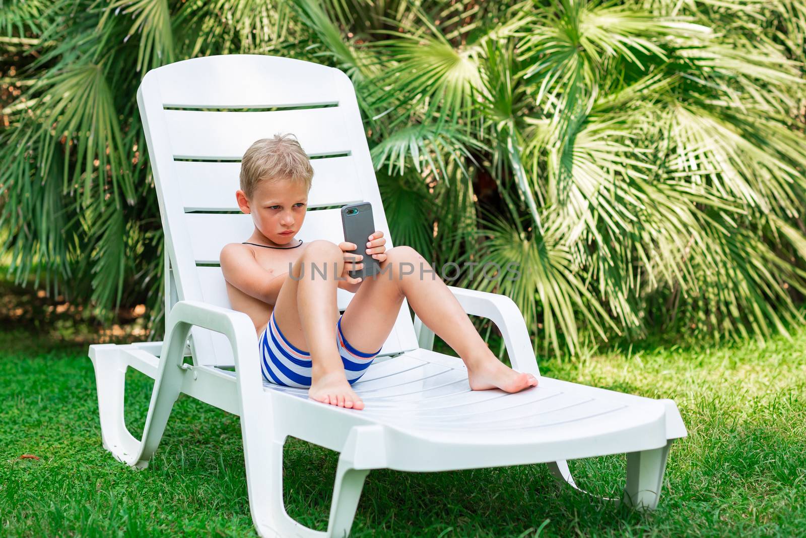 Boy playing games on the telephone. Gadget dependency disorder problem for kids during holiday vacation at the seaside concept