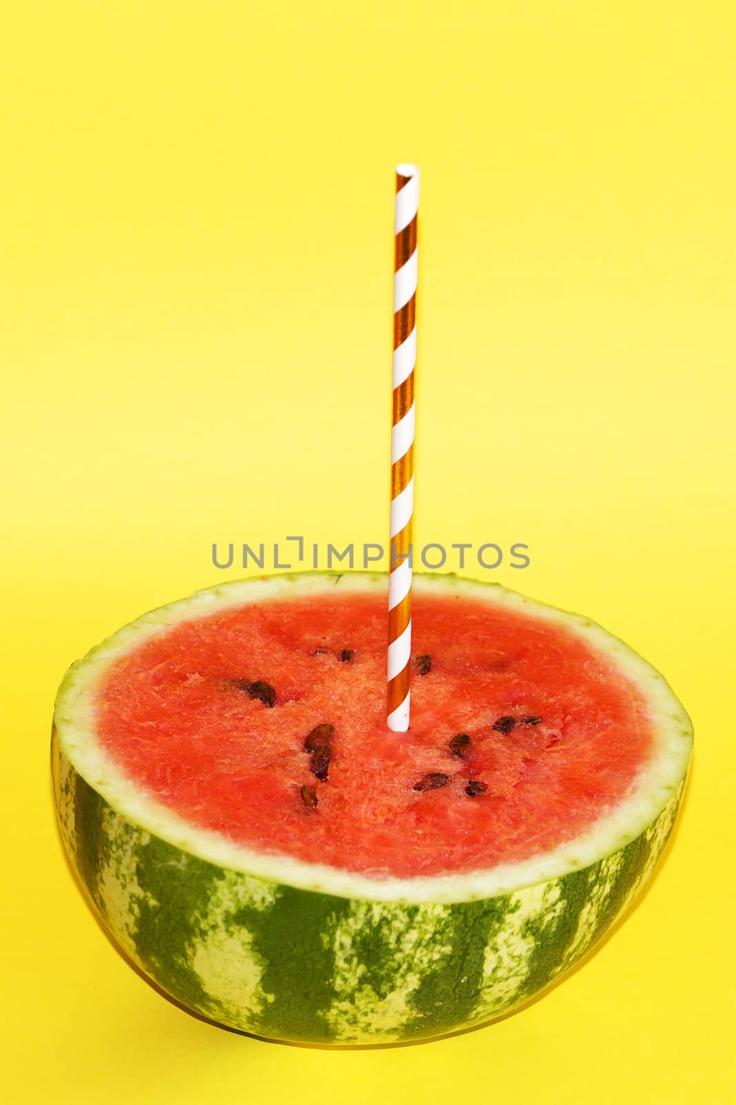 half watermelon with cocktail straw on yellow background, close-up