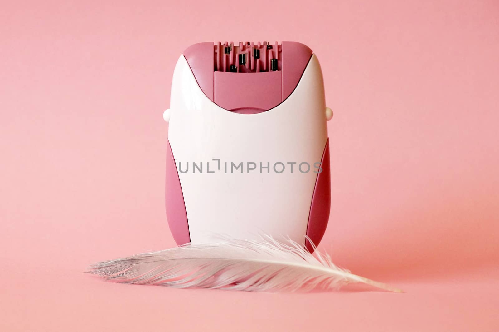 electric handheld epilator and feather on pink background close up