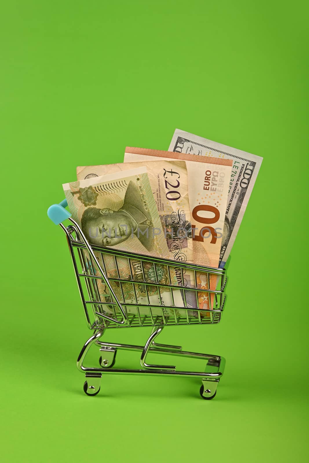 Close up several different world paper currency banknotes in small shopping cart over green background, low angle side view