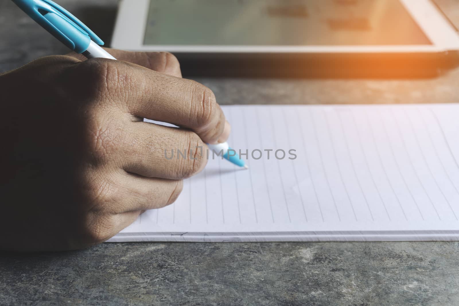 Close up of Men hands writing a paper note with a Tablet stay work from home or office To stop the spread of the coronavirus by yodsawai