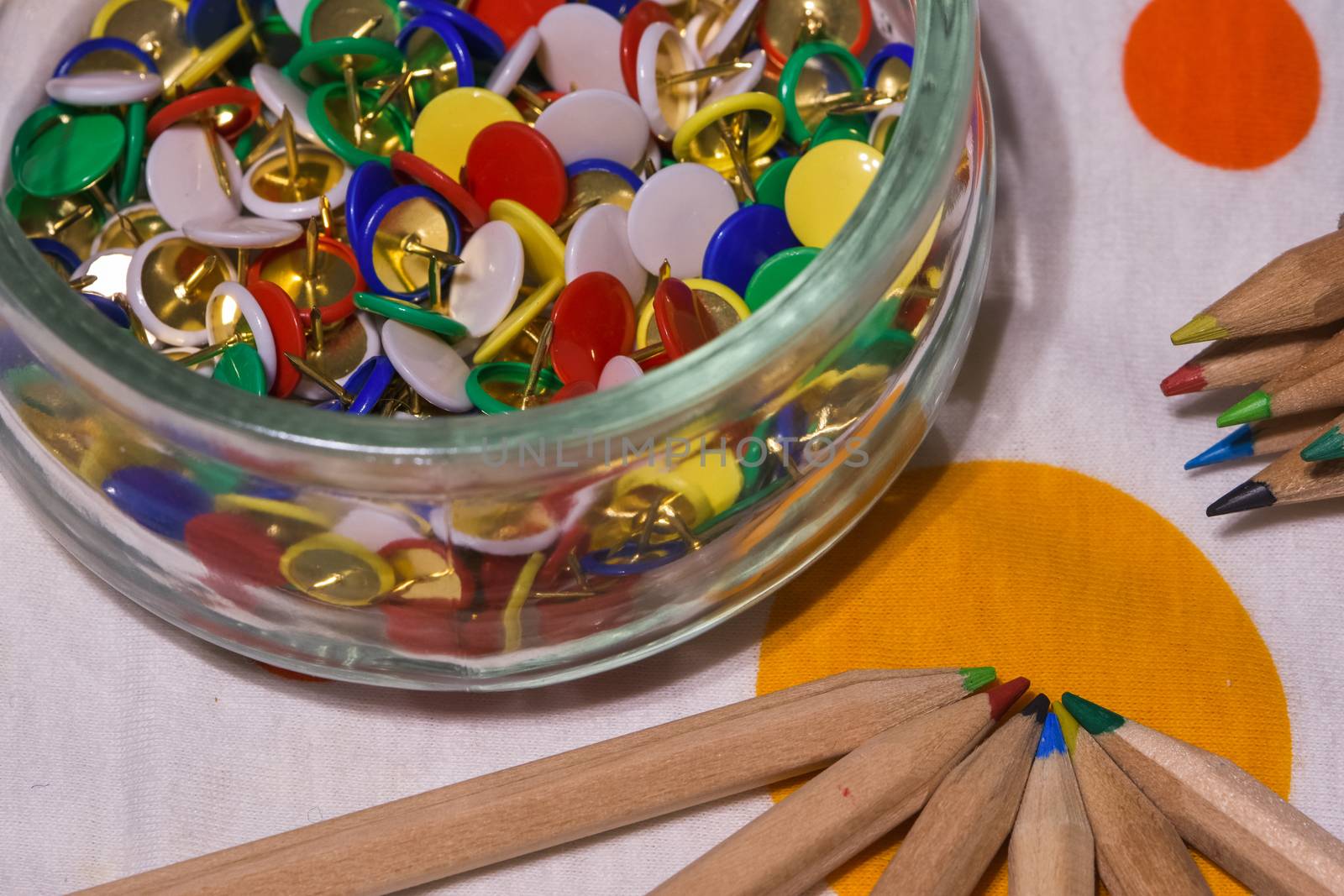 colored thumbtacks in a glass jar and colored pencils by brambillasimone