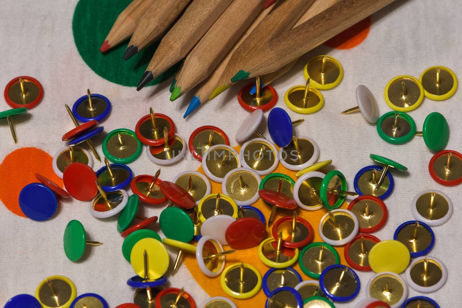 Thumbtacks and colored pencils scattered on a colored plane by brambillasimone