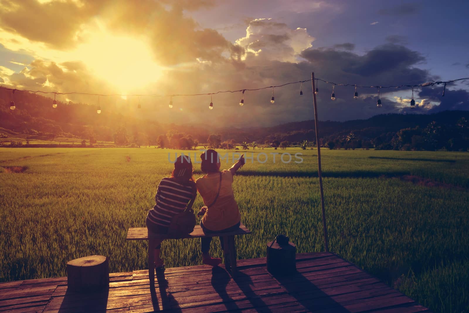 Two traveller enjoying a looking at sunset on rice field by ideation90