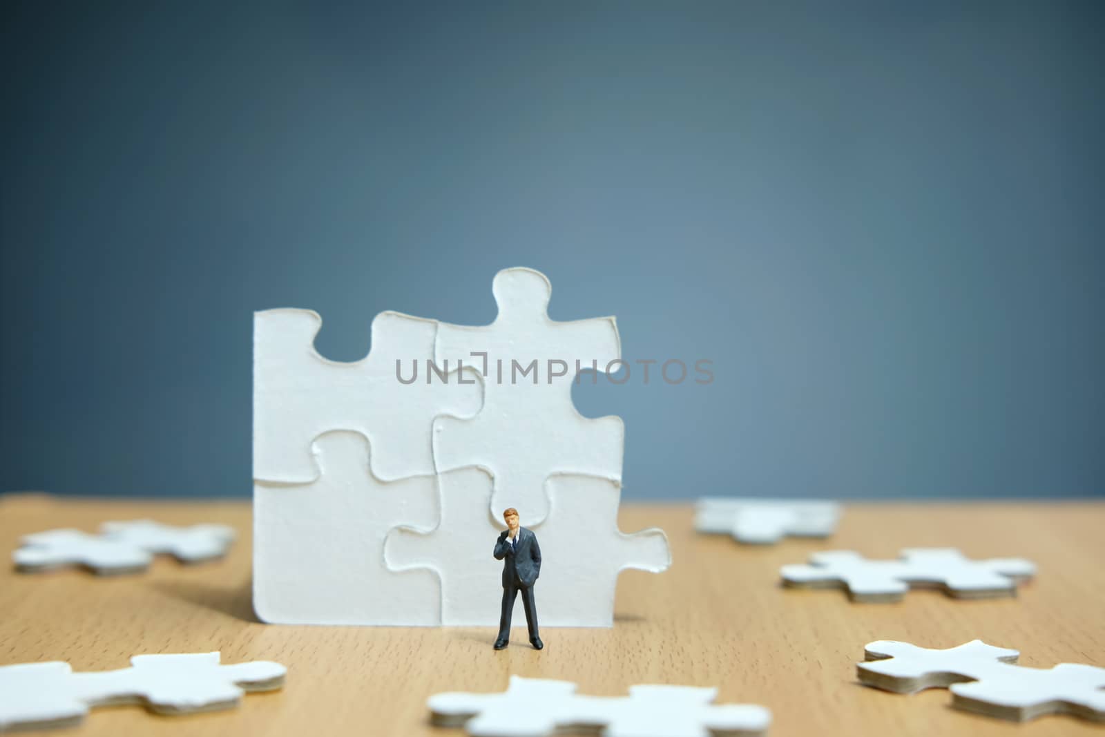 Conceptual photos of business strategies - Miniature entrepreneurs stand and think in front of 4 jigsaw puzzles that are arranged